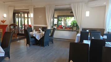 A restaurant with round tables, black chairs, and a view of the outdoors through large windows.