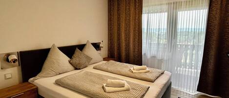 Ein Hotelzimmer mit einem großen Bett, zwei Kissen, einem Nachttisch, einer Holzkommode und einem Fenster mit Vorhängen.
