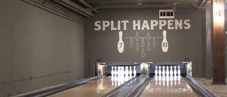 Een bowlingbaan met een bord waarop staat 'SPLIT HAPPENS' en bowlingpinnen die klaarstaan.