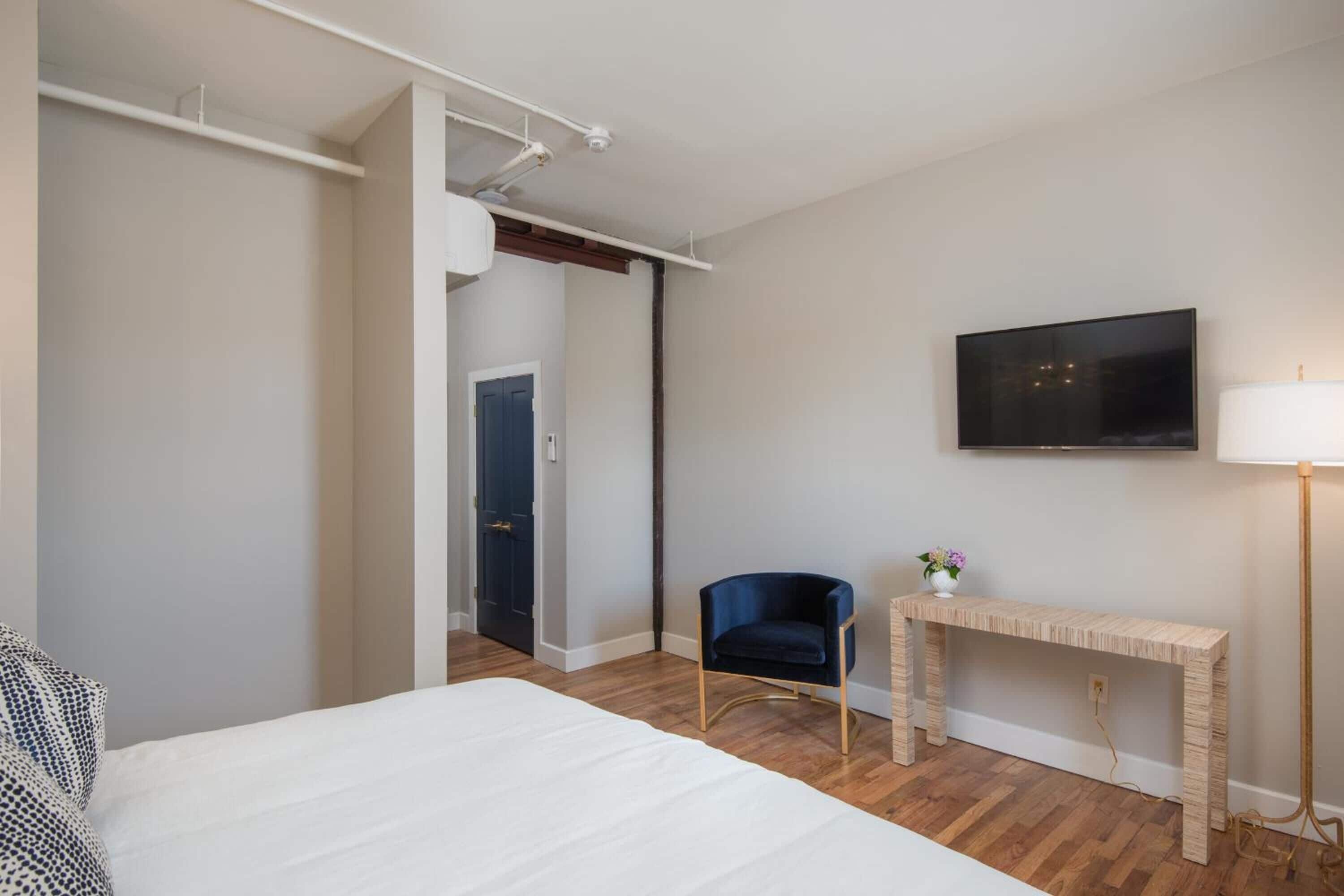 A hotel room with a bed, a desk, a chair, a TV, and a lamp.