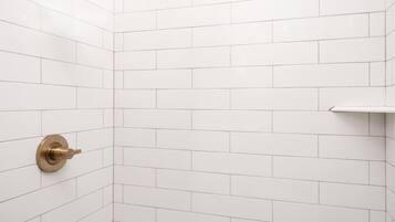 A shower with a gold showerhead and a wall-mounted control.