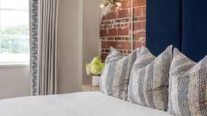 A bedroom with a brick wall, a dark blue headboard, and patterned pillows. - The Stricklin Hotel (Florence)