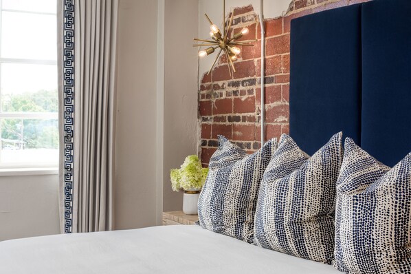 A bedroom with a brick wall, a dark blue headboard, and patterned pillows.