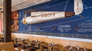 A restaurant with a large aircraft model mural on the wall, wooden tables, and chairs. - The Stricklin Hotel (Florence)