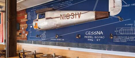 A restaurant with a large aircraft model mural on the wall, wooden tables, and chairs.