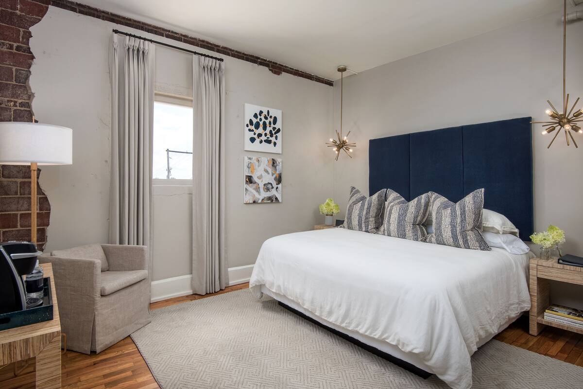 A bedroom with a large bed, a chair, a lamp, and artwork on the wall.