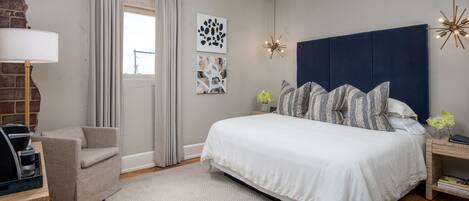 A bedroom with a large bed, a chair, a lamp, and artwork on the wall.