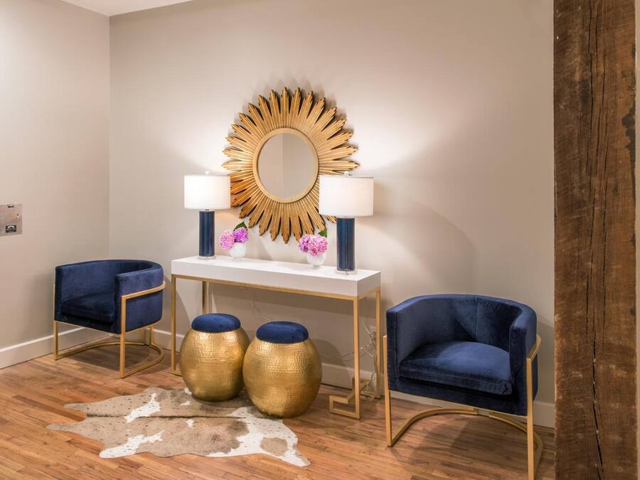 A room with a white console table, two blue chairs, a gold mirror, and a cowhide rug.