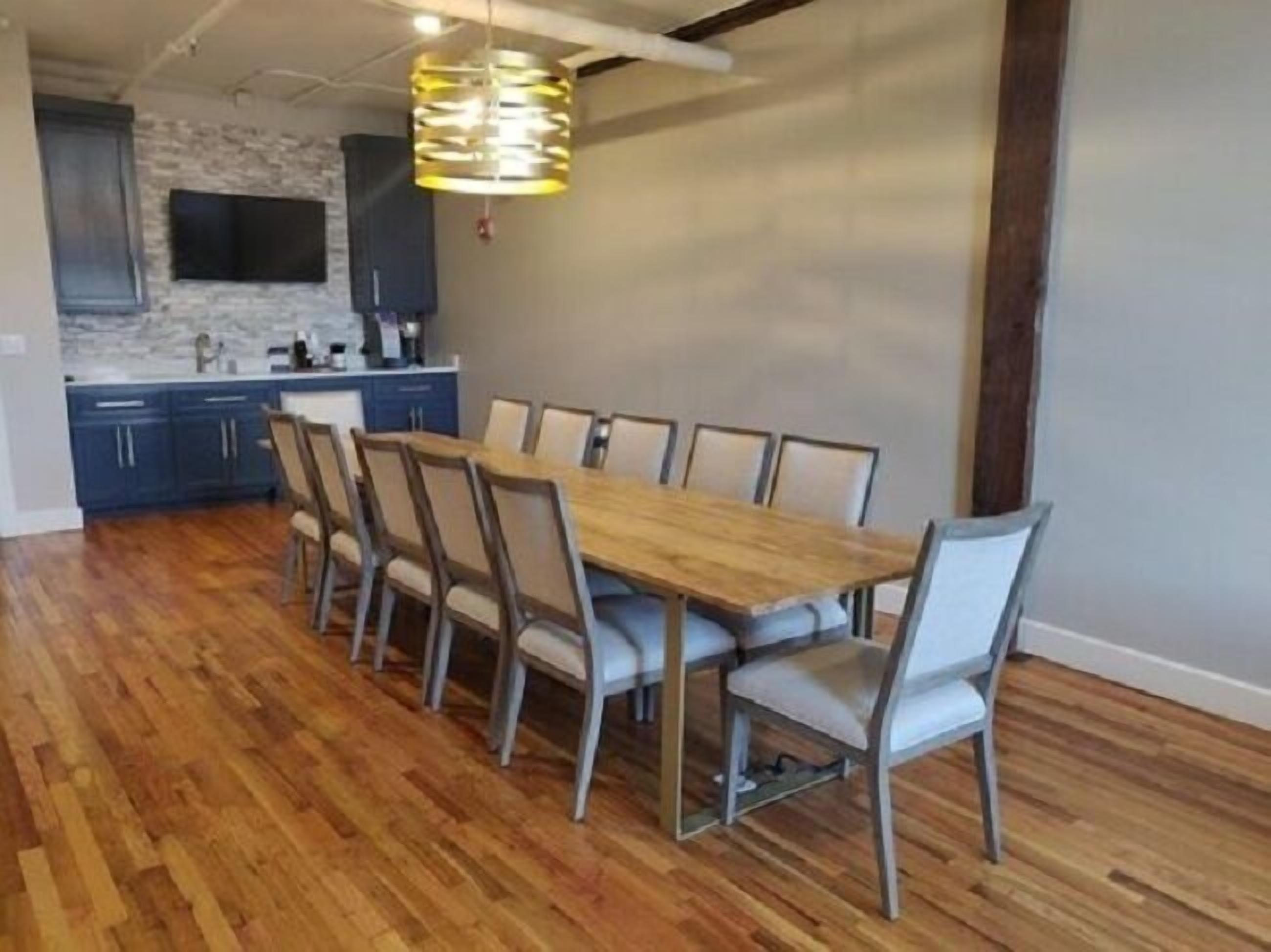 Un coin repas avec une table en bois et six chaises, un luminaire suspendu et une cuisine dotée de meubles bleus et d’un pare-feu en pierre.