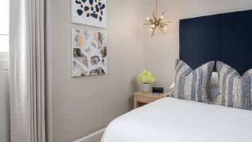 A bedroom with a bed, a nightstand, a wall-mounted light, and two abstract paintings.