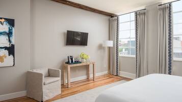 Une chambre d’hôtel avec un lit, un bureau avec une lampe, une chaise, une télévision et une fenêtre avec des rideaux.