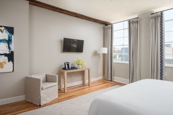A hotel room with a bed, a desk with a lamp, a chair, a TV, and a window with curtains.