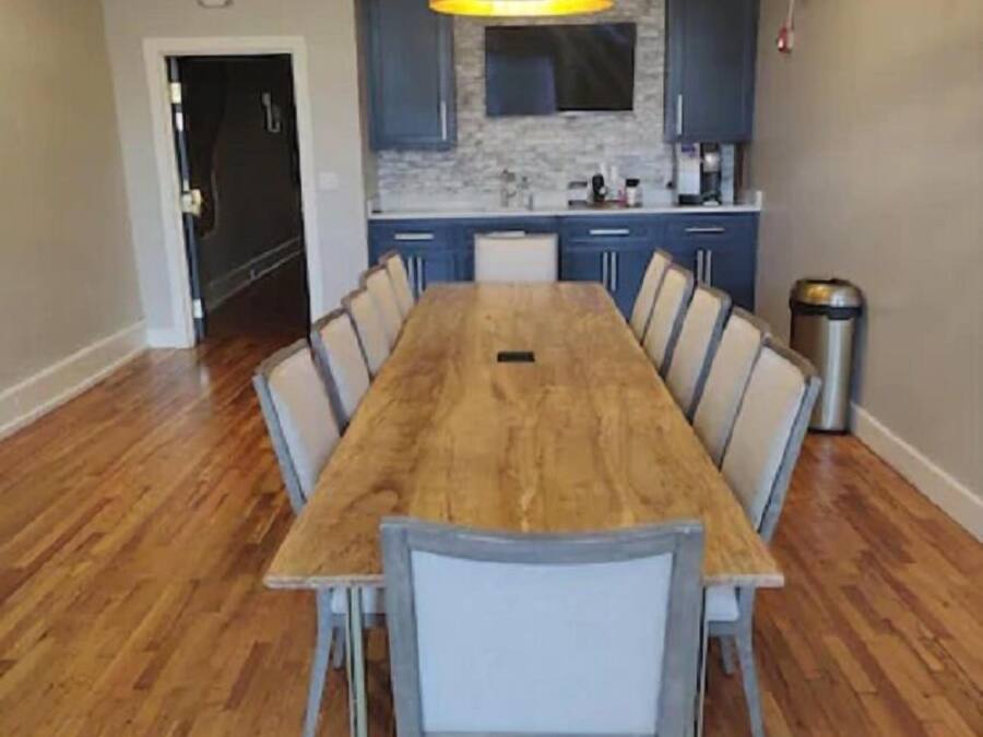 A dining area with a wooden table and chairs, a modern pendant light, and a kitchen in the background.