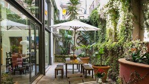 An outdoor patio with wooden tables and chairs, surrounded by potted plants and a large umbrella. - 4 Rooms Barcelona (Barcelona)