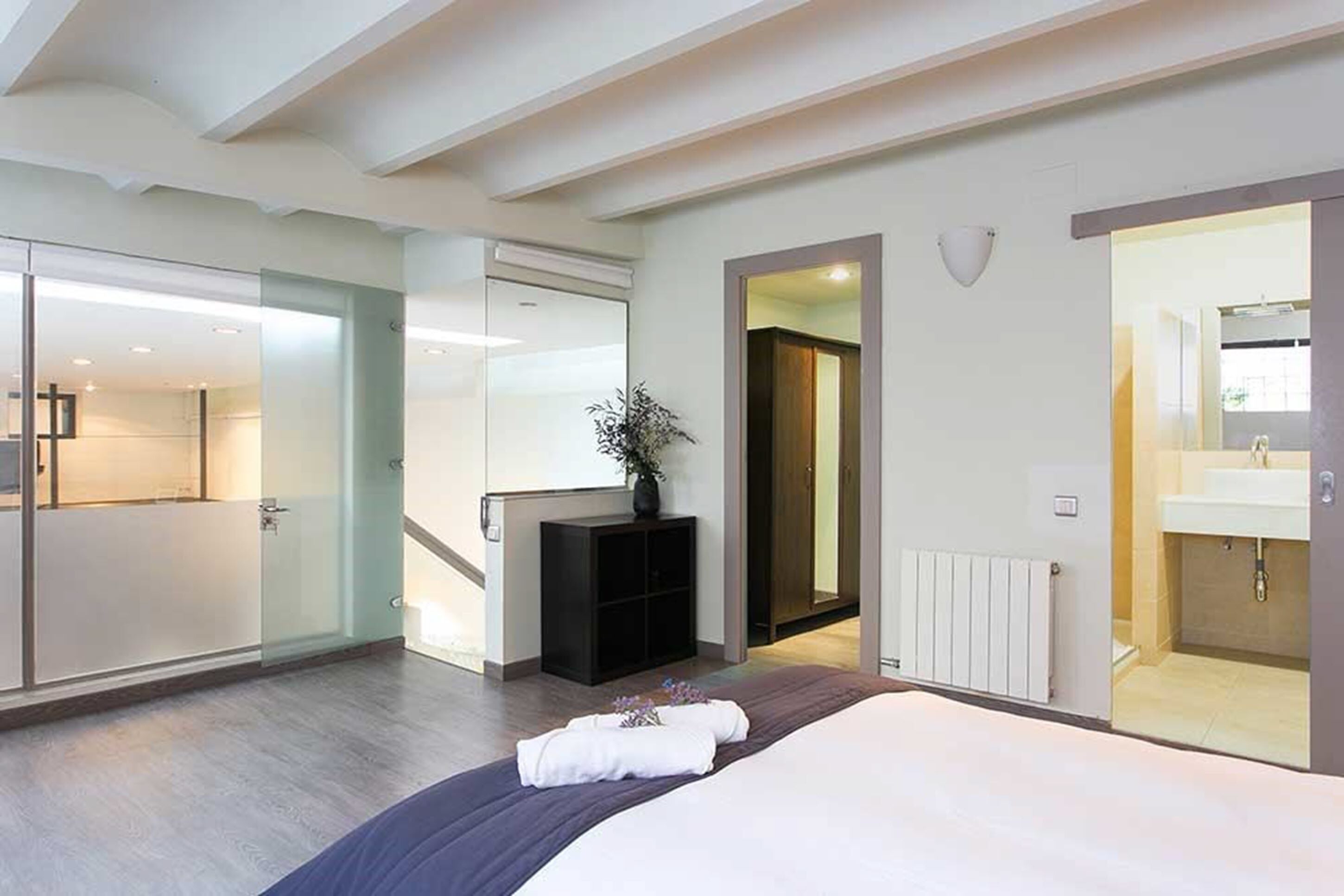 Habitación de hotel moderna con una cama grande, un vestidor amplio, un baño con un espejo grande y vistas a la ciudad.
