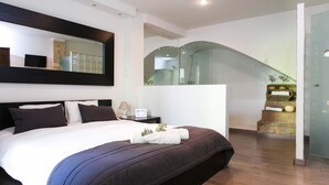 A modern hotel room with a large bed, a flat-screen TV, a bedside table with a lamp, and a glass-enclosed staircase. - 4 Rooms Barcelona (Barcelona)