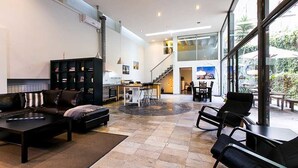 A spacious living area with a sofa, chairs, a coffee table, and a fireplace. There is a staircase leading to an upper level, and large windows providing natural light. - 4 Rooms Barcelona (Barcelona)