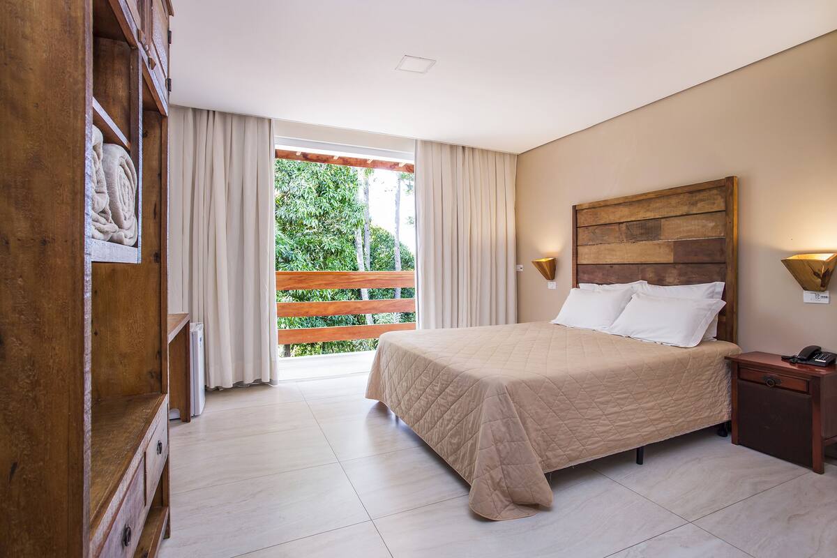 Un dormitorio con cama, cabecera de madera, lámparas de noche y vistas a un espacio exterior a través de una puerta corredera.
