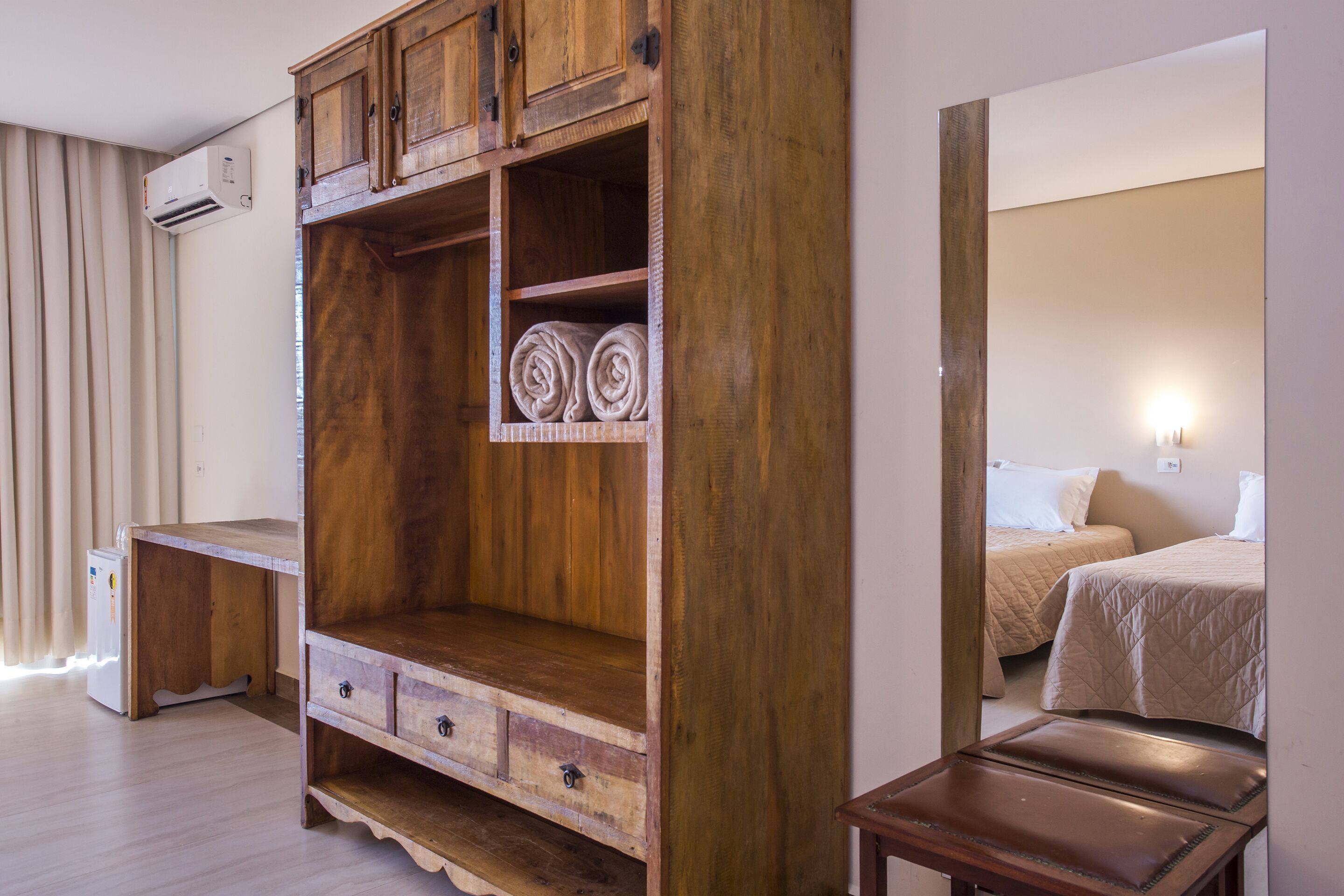 Un armario de madera con varios compartimentos, un escritorio pequeño y una cama con colcha acolchada.