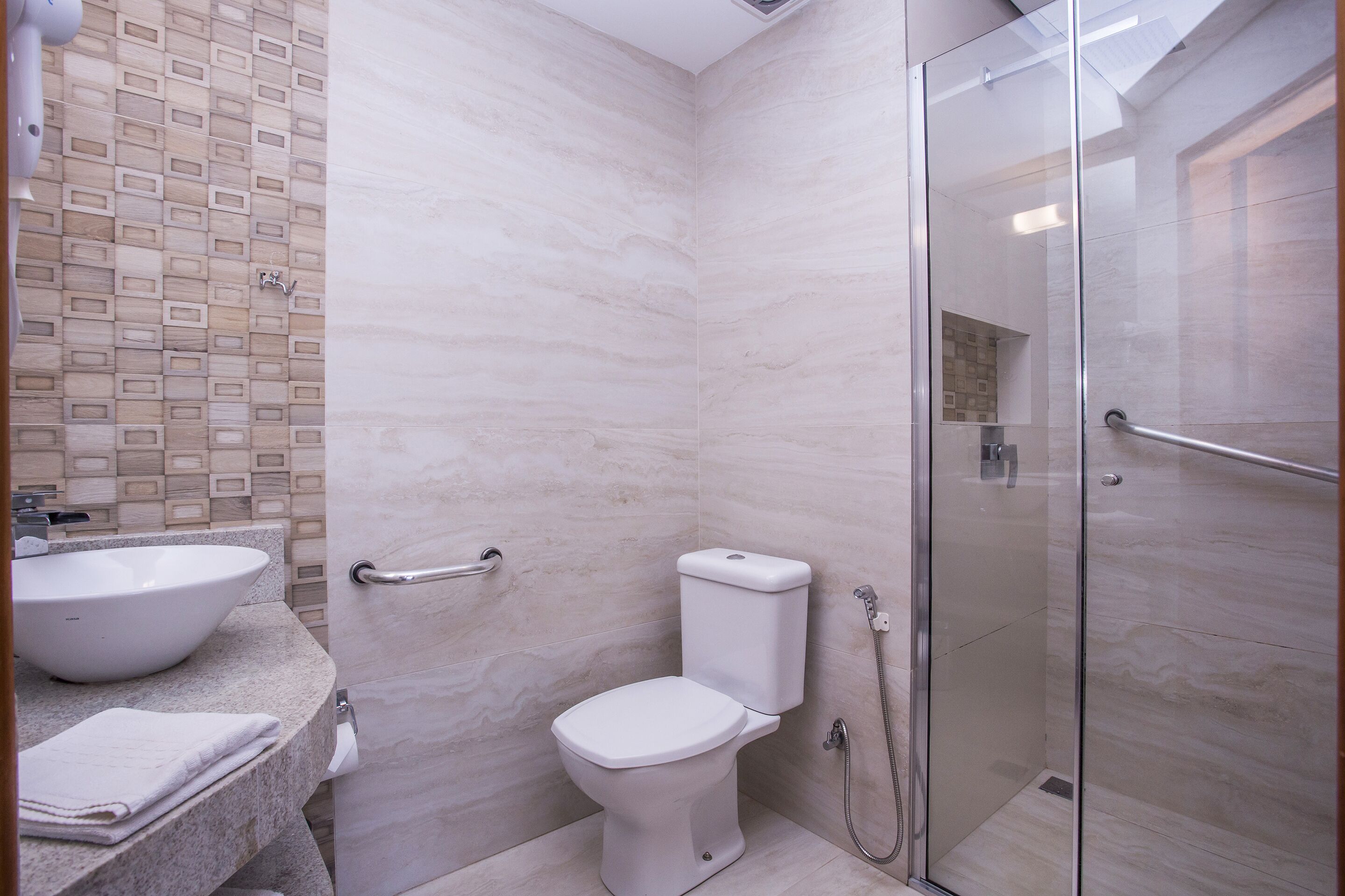 A modern bathroom with a glass shower enclosure, a white toilet, and a sink with a marble countertop.