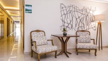 Um corredor com duas poltronas estofadas, uma mesa, uma obra de arte na parede e uma placa de sinalização.