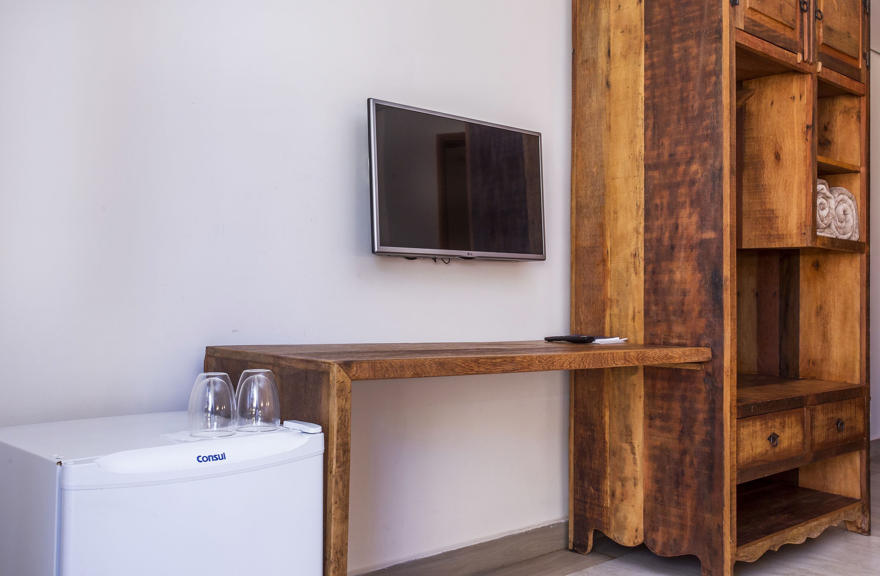 Una habitación con lavadora blanca, un escritorio de madera, un televisor montado en la pared y un mueble de madera con cajones.