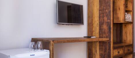 Una habitación con lavadora blanca, un escritorio de madera, un televisor montado en la pared y un mueble de madera con cajones.