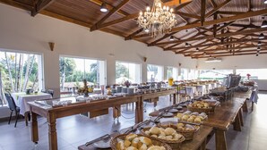 Una sala da pranzo spaziosa con lunghe tavolate, travi in legno e ampie finestre.