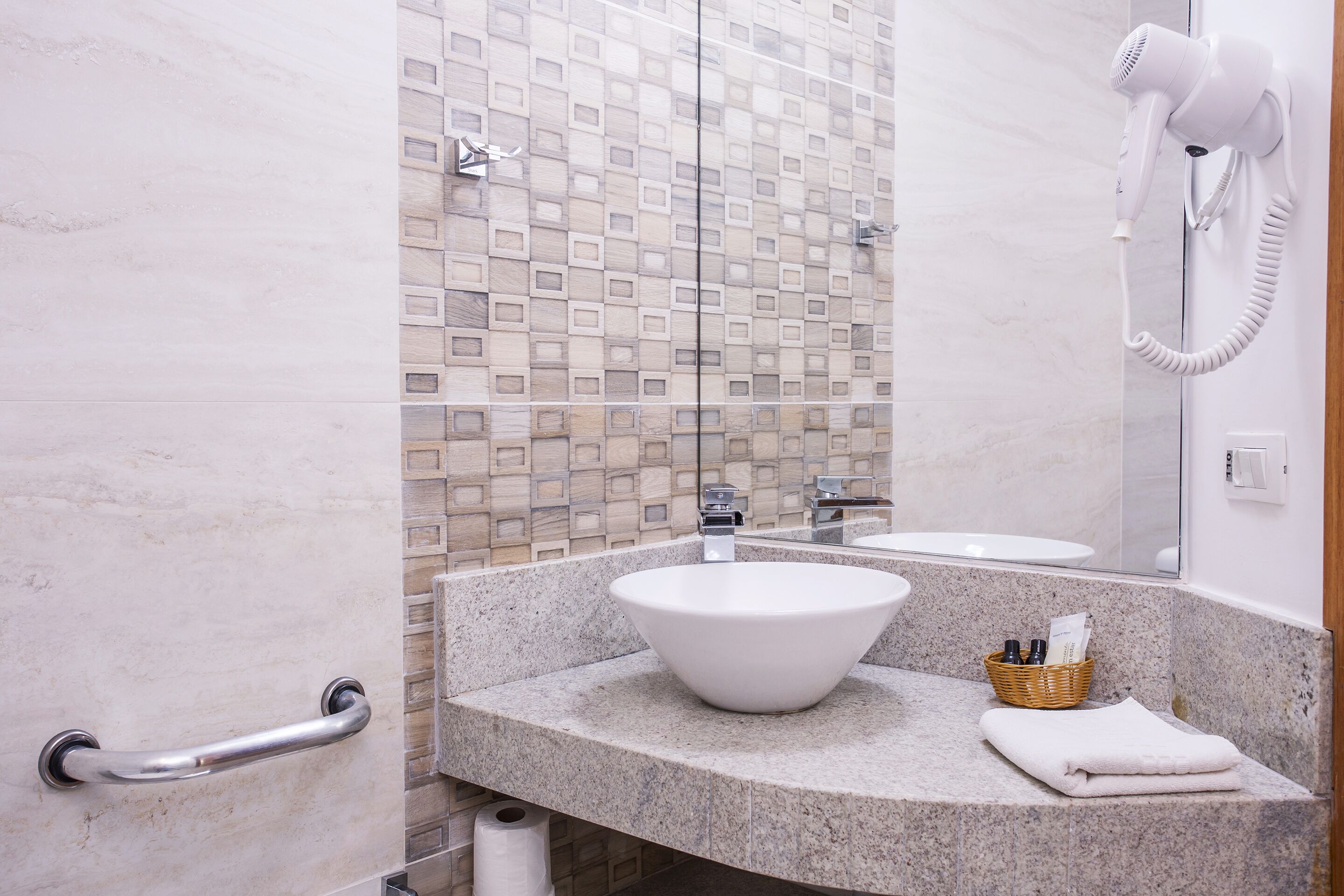 A bathroom with a white sink, a hairdryer mounted on the wall, a towel on the counter, and a handrail on the door.