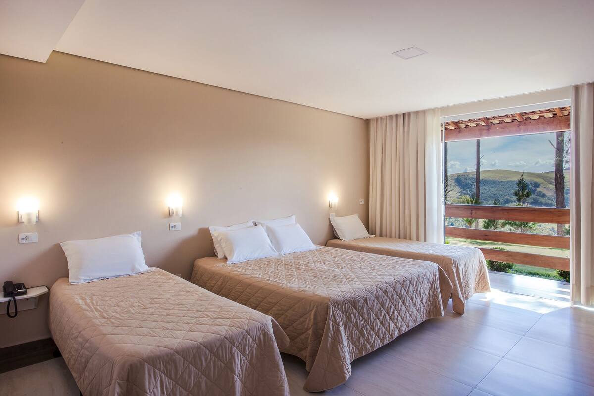 Habitación de hotel con dos camas, un teléfono en la mesita de noche y un ventanal con vistas a las colinas.