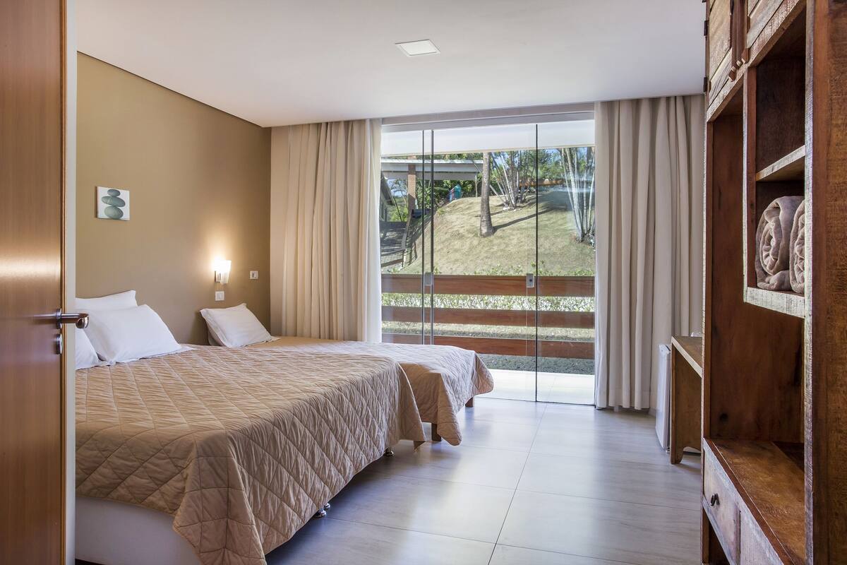 Habitación de hotel con dos camas, un armario de madera, un amplio ventanal corredero al exterior y una pequeña obra de arte en la pared.