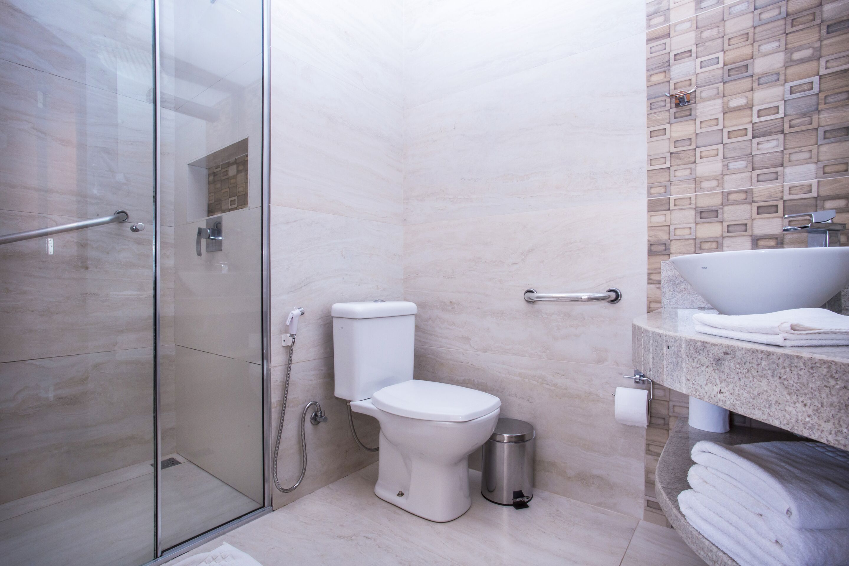 A modern bathroom with a glass shower enclosure, a toilet, a sink with a marble countertop, and a trash can.