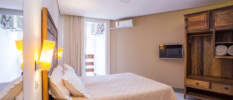 Habitación de hotel con cama, lámparas de noche, televisor, aparador de madera y unidad de aire acondicionado.
