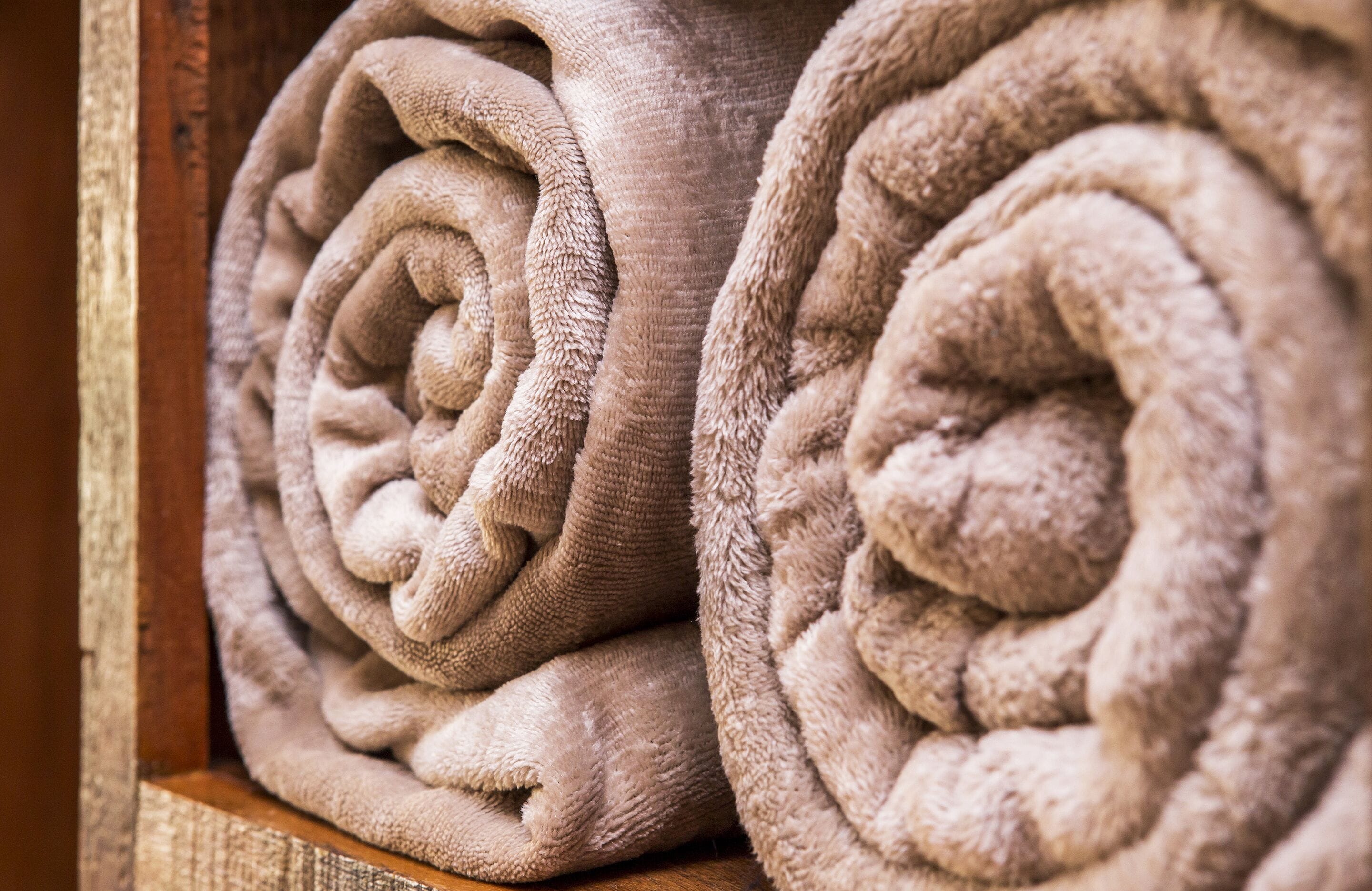 A close-up of neatly rolled beige towels stacked in a wooden container.