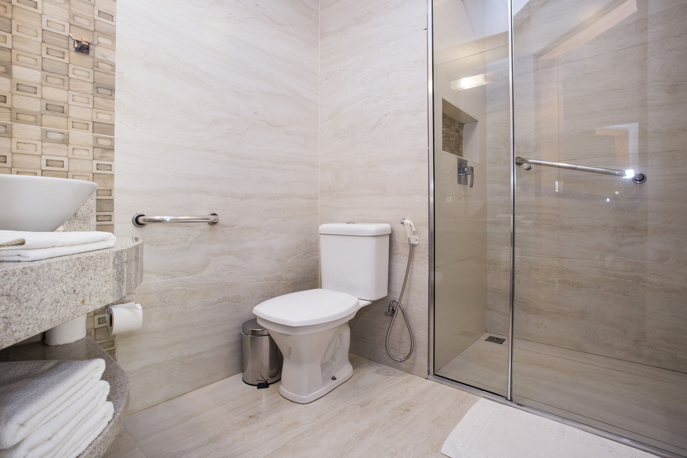 Un baño moderno con cabina de ducha de vidrio, inodoro, lavabo con encimera de mármol y un cubo de basura.