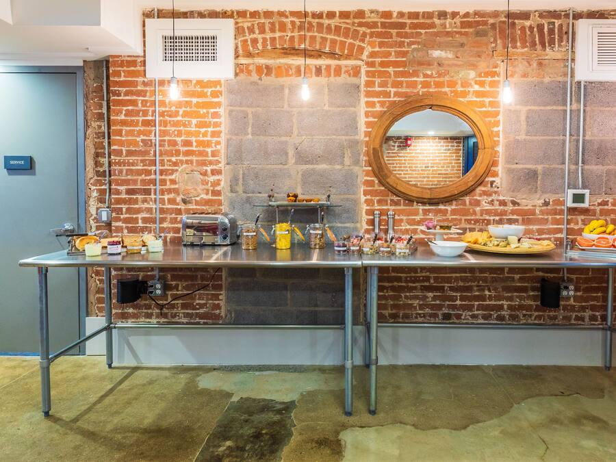 A breakfast bar with various food items and a toaster, set against a brick wall with a round mirror above.