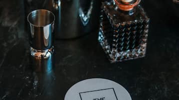 Una zona de bar con un shaker metálico, un vaso pequeño y un posavasos con el texto 'THE GEORGE'.