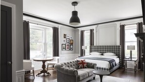 A bedroom with a bed, a grey sofa, a round table, and a chandelier. - The George (Montclair)