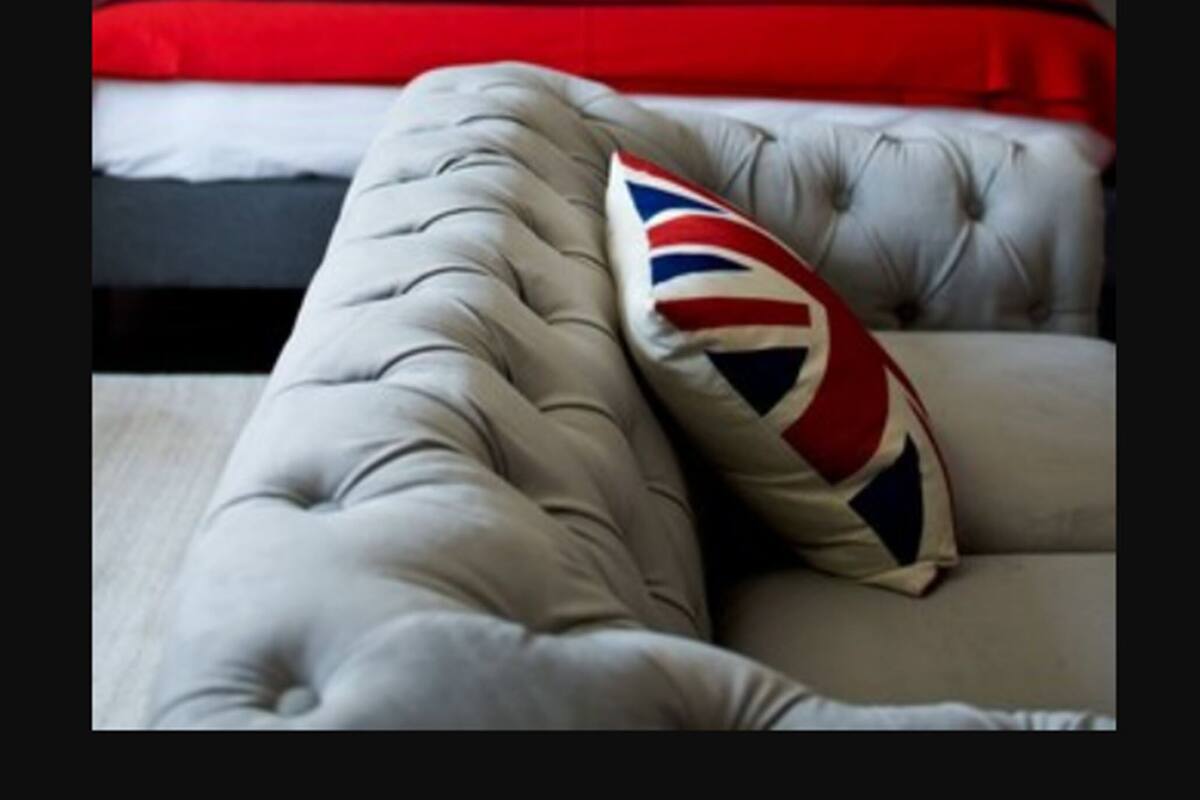Una cama con cabecera a cuadros rojos y blancos, almohada blanca y roja, y un banco tapizado en gris.