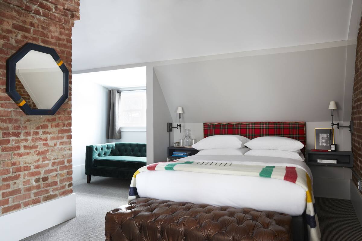 Un dormitorio con pared de ladrillo, una cama grande con manta colorida, un sofá verde y un cabecero rojo a cuadros.