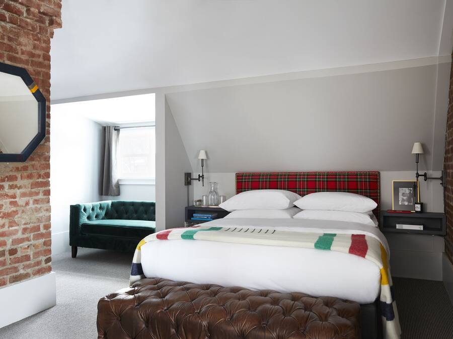 A bedroom with a brick wall, a large bed with a colorful blanket, a green sofa, and a red plaid headboard.