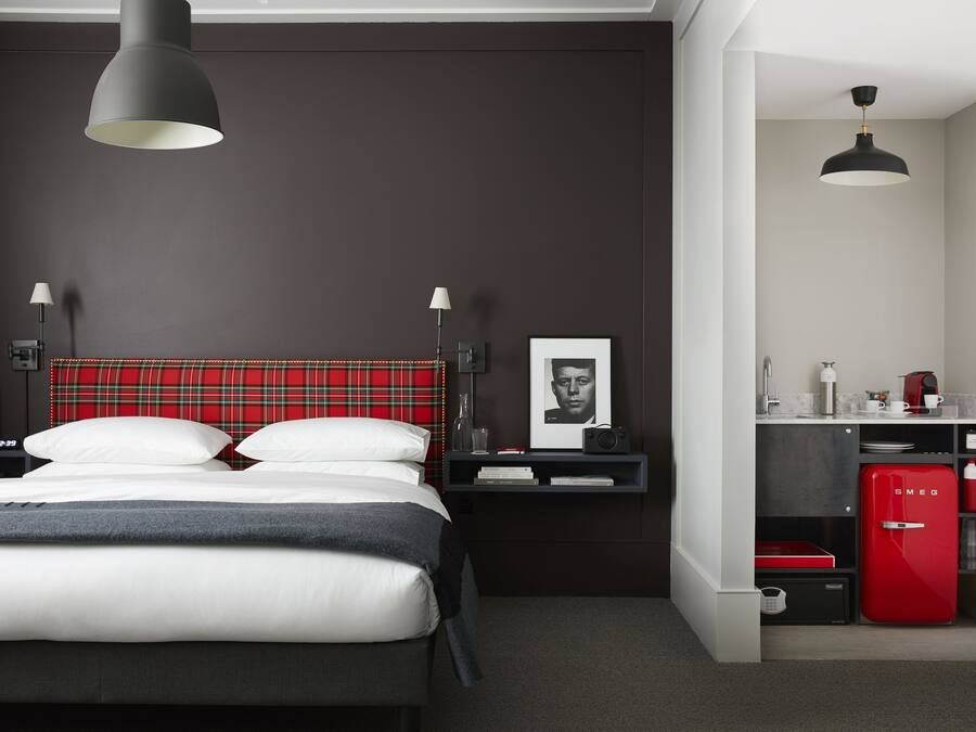 Ein modernes Schlafzimmer mit einem Bett, Nachttischen, einem roten Kühlschrank und einer kleinen Küchenzeile.