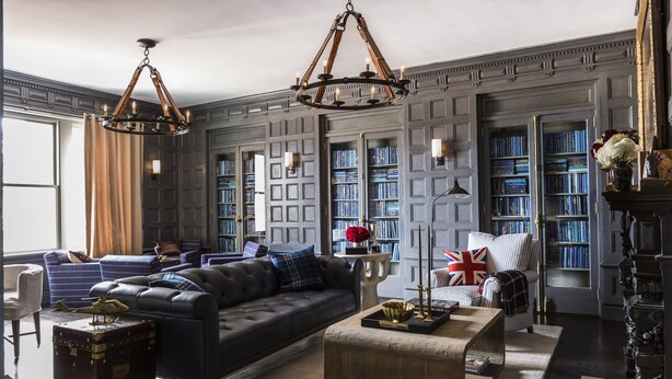 A living room with a dark leather sofa, a wooden coffee table, and a bookshelf filled with books. - The George (Montclair)