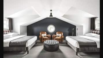 A bedroom with two beds, a round table, and two leather armchairs.