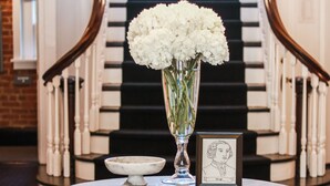 A marble table with a vase of white flowers, a framed picture, and a small bowl. - The George (Montclair)