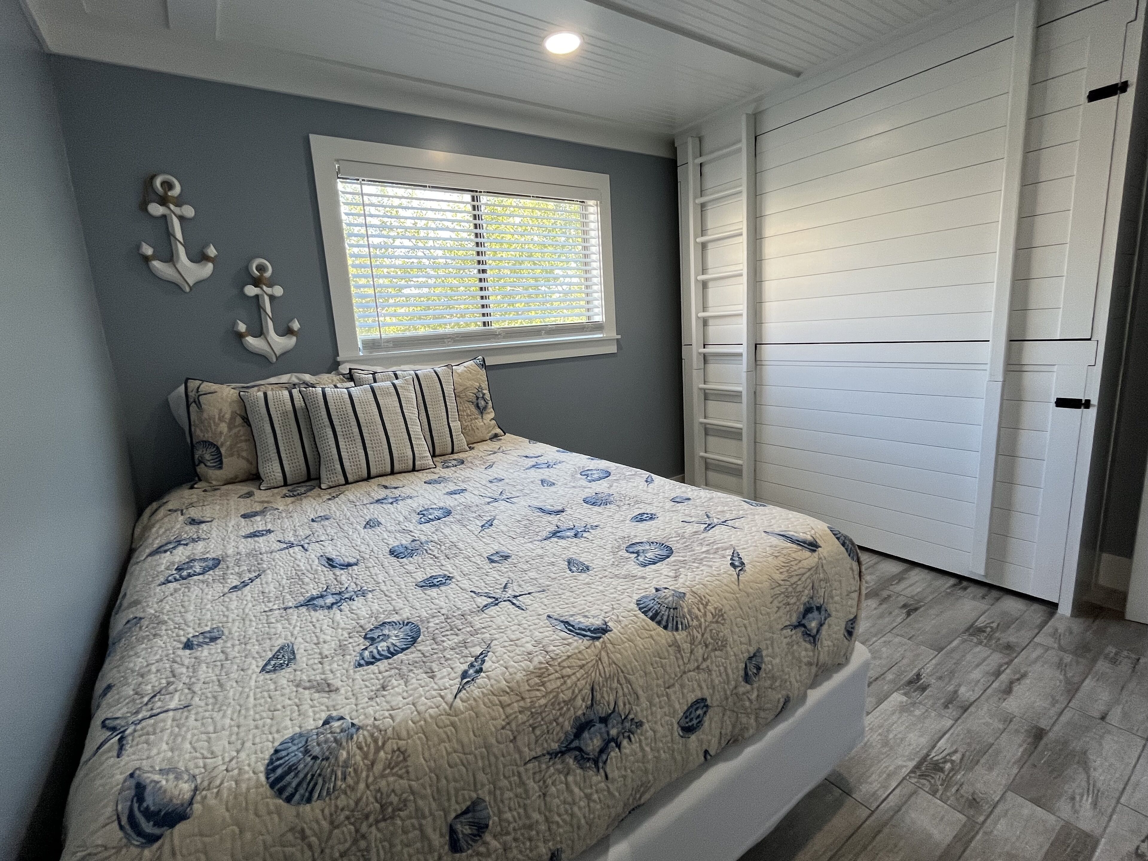 A bedroom with a bed, a window with blinds, a white closet, and a wall with decorative anchors.