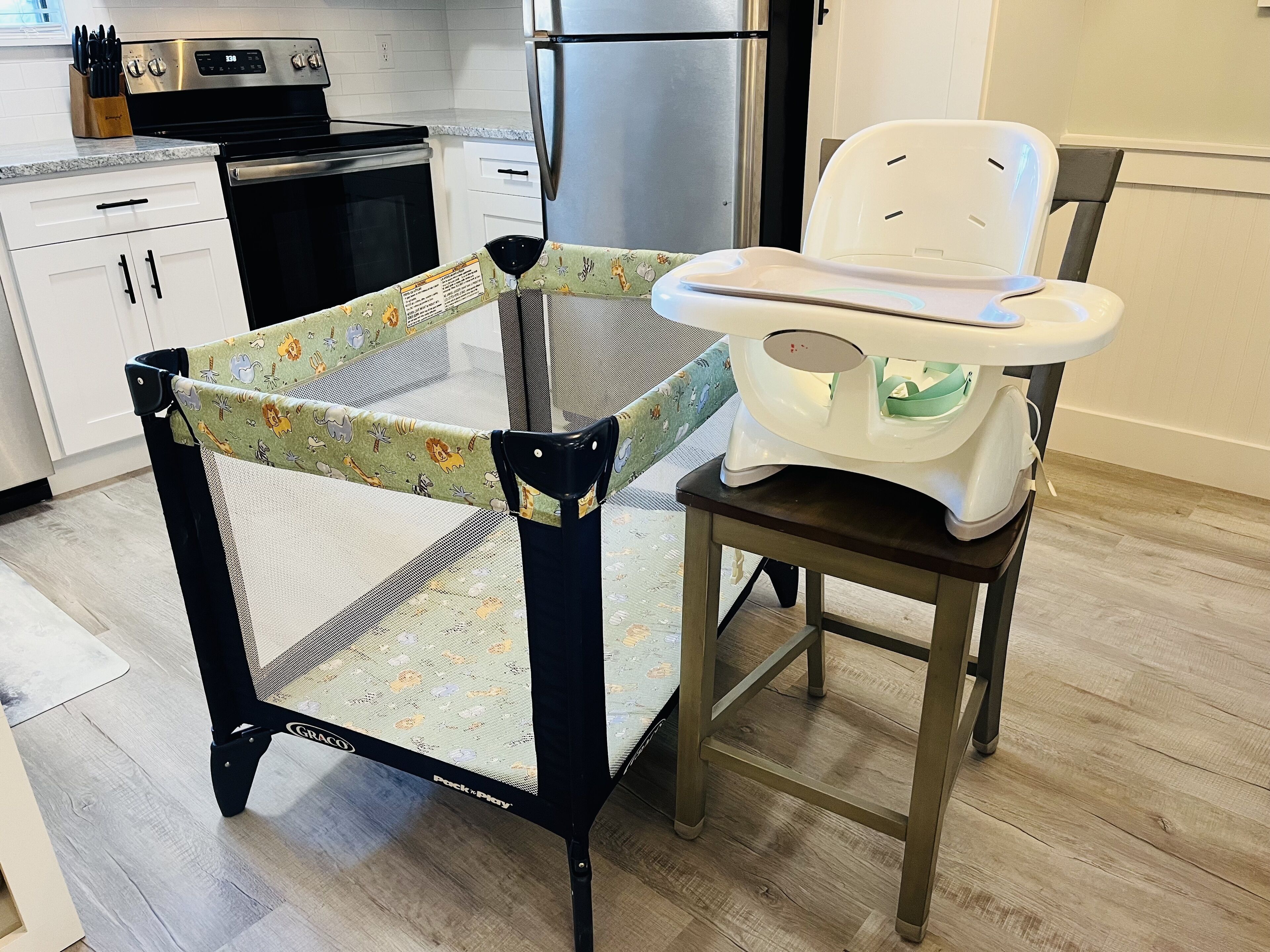 A kitchen with a baby playpen, a baby rocker, and a refrigerator.