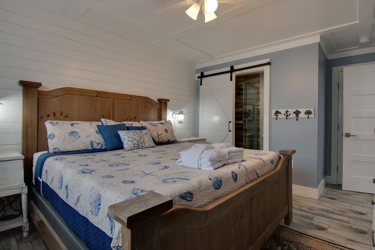A bedroom with a wooden bed, a nightstand, a wall-mounted lamp, and a door with a towel rack.