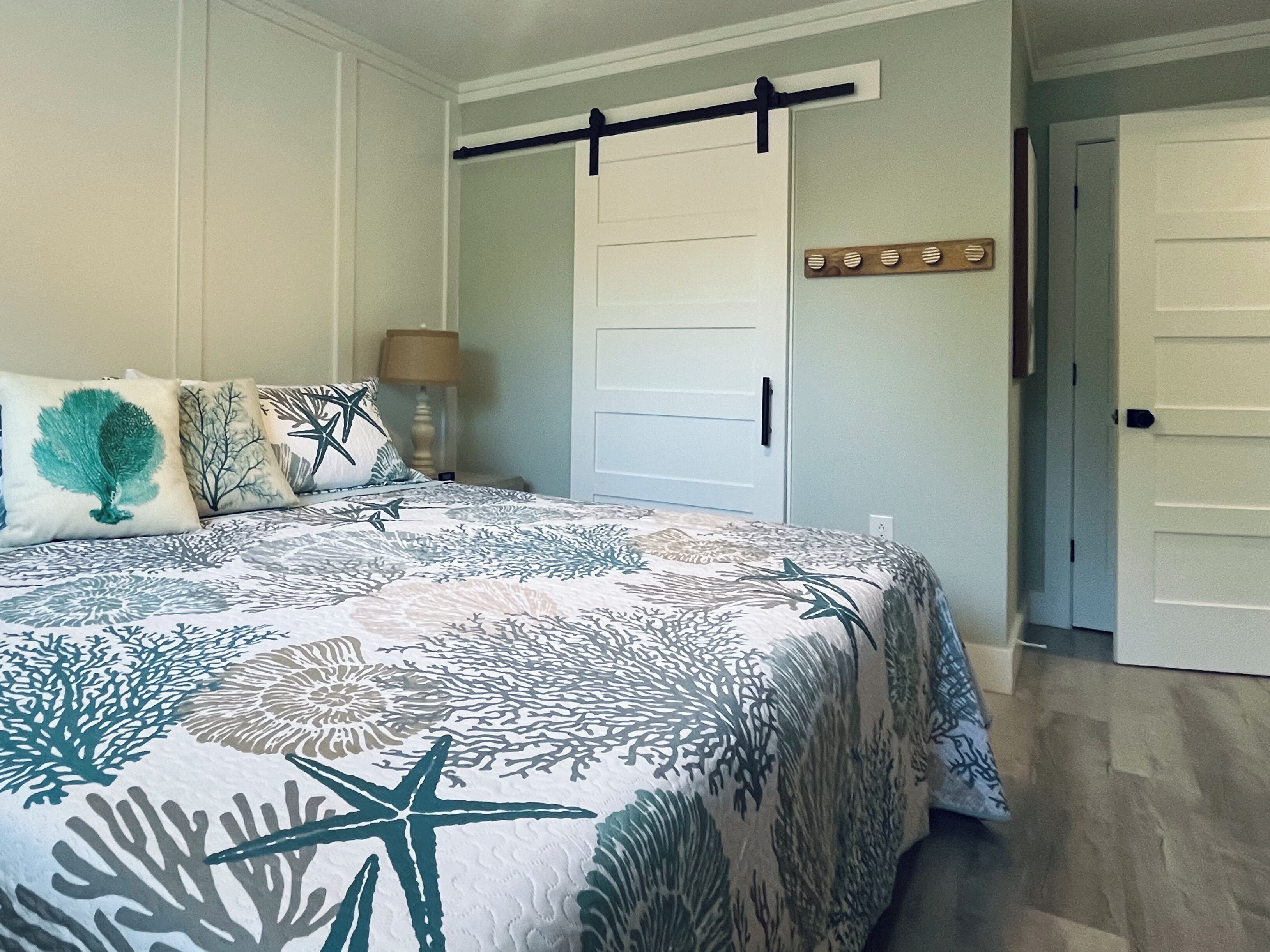 Une chambre à coucher comprenant un lit, une table de chevet, une lampe, une porte et un élément décoratif fixé au mur.