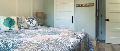 A bedroom with a bed, a nightstand, a lamp, a door, and a wall-mounted decoration.